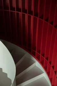 Modern, minimalist white staircase with a red painted wooden railing.