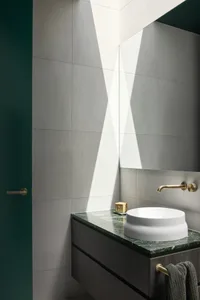 Modern bathroom with concrete walls and a round white sink on a green marble countertop.
