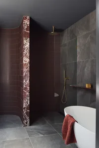 A modern luxury bathroom featuring a white bathtub with a red towel, dark grey marble tiles, and a freestanding bathtub.