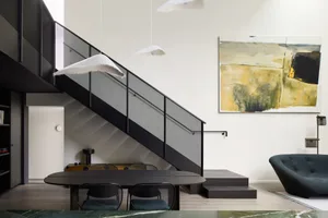 A modern minimalist dining area with a black metal staircase and a large abstract painting on the wall.