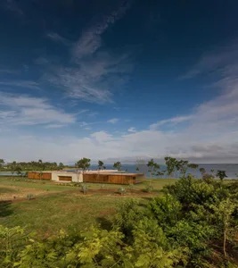 A modern residential home with a wooden and concrete exterior, surrounded by lush greenery and a serene lake.