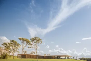 Modern residential home with a wooden exterior and concrete accents, set against a clear blue sky with scattered clouds.