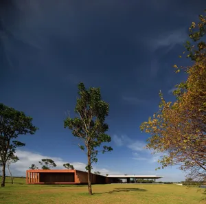 A modern house with a wooden exterior surrounded by green lawn and trees against a clear blue sky.
