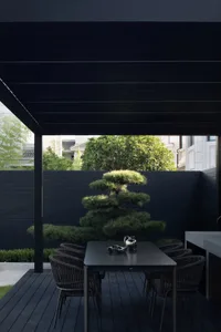 A modern outdoor dining area featuring a dark wooden deck with a black pergola and a black table surrounded by black chairs, 