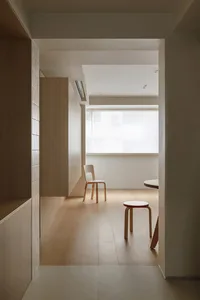 A minimalist living room featuring wooden flooring, a white chair, and a small table.