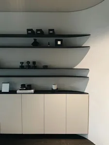 Modern minimalist interior with black glass shelves, white cream cabinets, and a concrete backdrop.