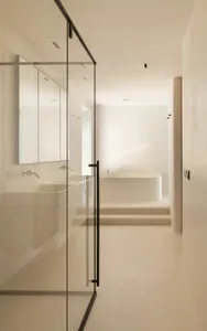Minimalist modern bathroom with glass walls, white fixtures, and steps leading to a freestanding bathtub.
