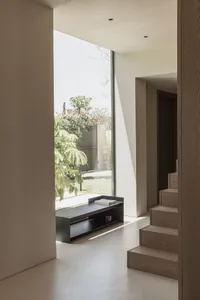 Minimalist interior design featuring wooden stairs, a sleek black bench, and natural light from a large window.