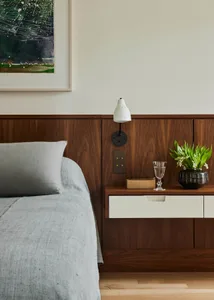 Modern minimalist bedroom featuring wood paneling, a grey bedspread, and a nightstand with a plant, glass, and book