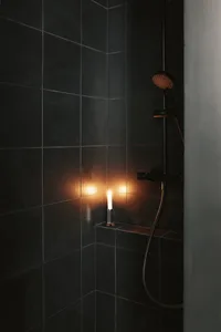 A minimalist bathroom with black tiles and a glowing candle.