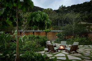 A serene outdoor space featuring modern furniture, natural stone pathways, bamboo fencing, and lush greenery.