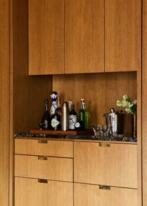 A modern home bar with wooden cabinets and shelves storing various bottles of liquor and glasses.