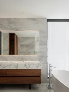 Modern bathroom featuring marble countertop and wood vanity with a freestanding bathtub and large window.