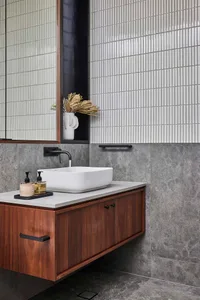 Modern bathroom with a white vessel sink, walnut vanity, and tiled walls.