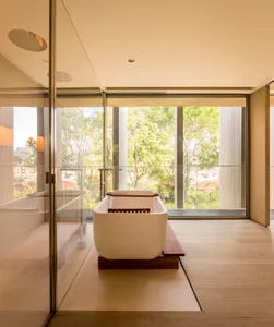 A modern bathroom featuring a white freestanding bathtub placed on a wooden platform against a floor-to-ceiling window with a