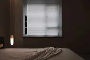 A neatly arranged bedroom with a bed and white bedding, illuminated by a hanging light fixture and natural light from a windo