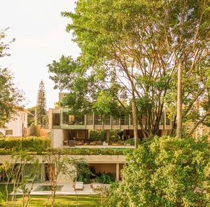 Modern residential house with glass exterior framed by lush greenery and trees.