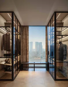 A well-organized modern minimalist closet featuring glass walls and a bench with a view of the cityscape.