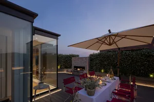 Outdoor dining area with red folding chairs, white tablecloth, and umbrella on a wooden deck at dusk.