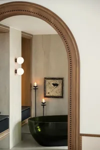 A minimalist bathroom with a black ceramic freestanding tub, candles, and a framed abstract painting.
