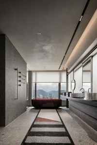 A modern bathroom featuring a red freestanding bathtub, concrete walls, and marble accents, with a view of mountains and a ci