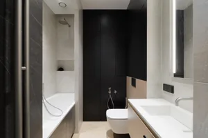 A modern bathroom with white ceramic tiles and black accents, featuring a white bathtub, white toilet, and white sink with a 