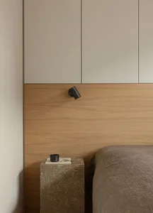A minimalist bedroom featuring a wooden headboard and a bed with a neutral-colored comforter, set against a wall with built-i