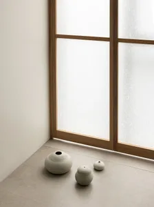 Three minimalist ceramic vases sitting on a floor by a window, creating a serene and modern aesthetic.