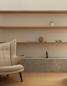 A minimalist living room with wooden concrete shelves, a beige upholstered armchair, and decorative objects.