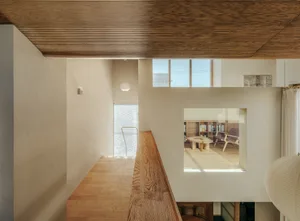 A modern residential interior with wooden accents, featuring a balcony area and a window view into a living space.