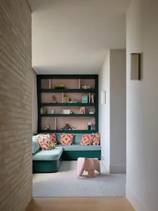 A modern children's playroom featuring built-in shelves with toys and books, a cozy seating area, and a pink elephant toy on 