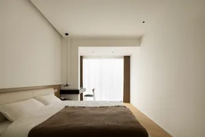 A minimalist bedroom with neutral-toned furniture, white bed linen, and a simple design.