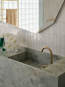 Modern bathroom featuring a marble sink and countertop with a brass faucet and orchid flowers in a green vase.