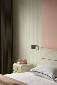Minimalist bedroom with a patterned upholstered headboard and white bed, featuring a soft pink pillow and a green bedside dra