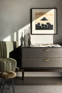 Modern living room with wooden furniture, a woven stool, and a framed artwork.