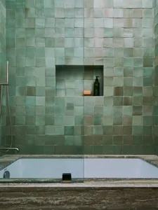 Modern bathroom with green ceramic tiles and a white bathtub. Green tiles cover the walls, creating a serene and stylish atmo