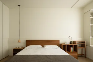 A minimalist bedroom featuring a wooden bed with white bedding and a pendant light hanging from the ceiling.