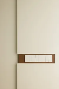 A minimalist light switch panel with a wooden frame and white plastic buttons mounted on a beige wall.