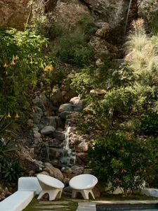 A peaceful garden scene featuring a minimalist waterfall surrounded by lush greenery and stones.
