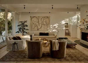 A minimalist living room with beige sofas, brown armchairs, and a fireplace, featuring a geometric abstract painting and a la