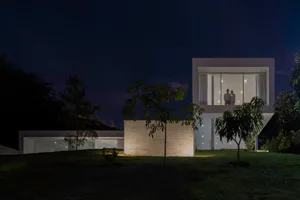 A modern residential building with concrete exterior and large windows at night.