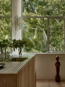 Modern residential bathroom featuring wooden furniture, marble countertop, and large windows overlooking lush greenery.