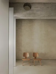 Two minimalist chairs made of wood in front of a concrete wall.
