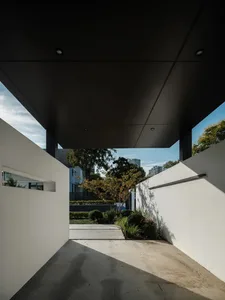 A modern entryway with concrete flooring, glass walls, and lush greenery and trees.
