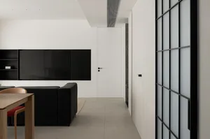 A modern minimalist apartment featuring concrete flooring, a large black wall-mounted TV, and a black couch in a spacious liv