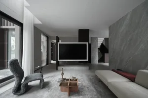 A modern living room featuring concrete walls and flooring, minimalist furniture, and a large window.