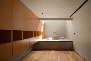 Minimalist living room with wooden furniture and floor, featuring a low table and cushions.