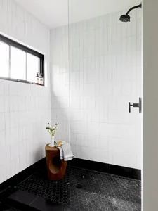A modern bathroom with white tiled walls and black hexagonal floor tiles, featuring a shower stall.