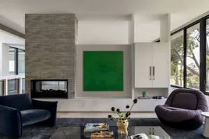 A modern contemporary living room featuring a green canvas art piece, dark blue and purple plush chairs, a glass coffee table