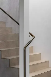 Modern wooden staircase with a bronze handrail and mesh guard.